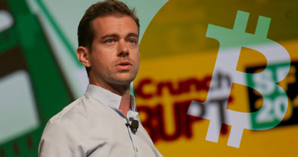 A man in a white shirt speaks on stage with conference branding and a large Bitcoin symbol overlayed on the image.