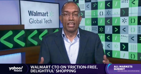 A man in a suit speaks during a Yahoo! Finance segment, with “Walmart Global Tech” and digital icons in the background, discussing friction-free shopping at the All Markets Summit.