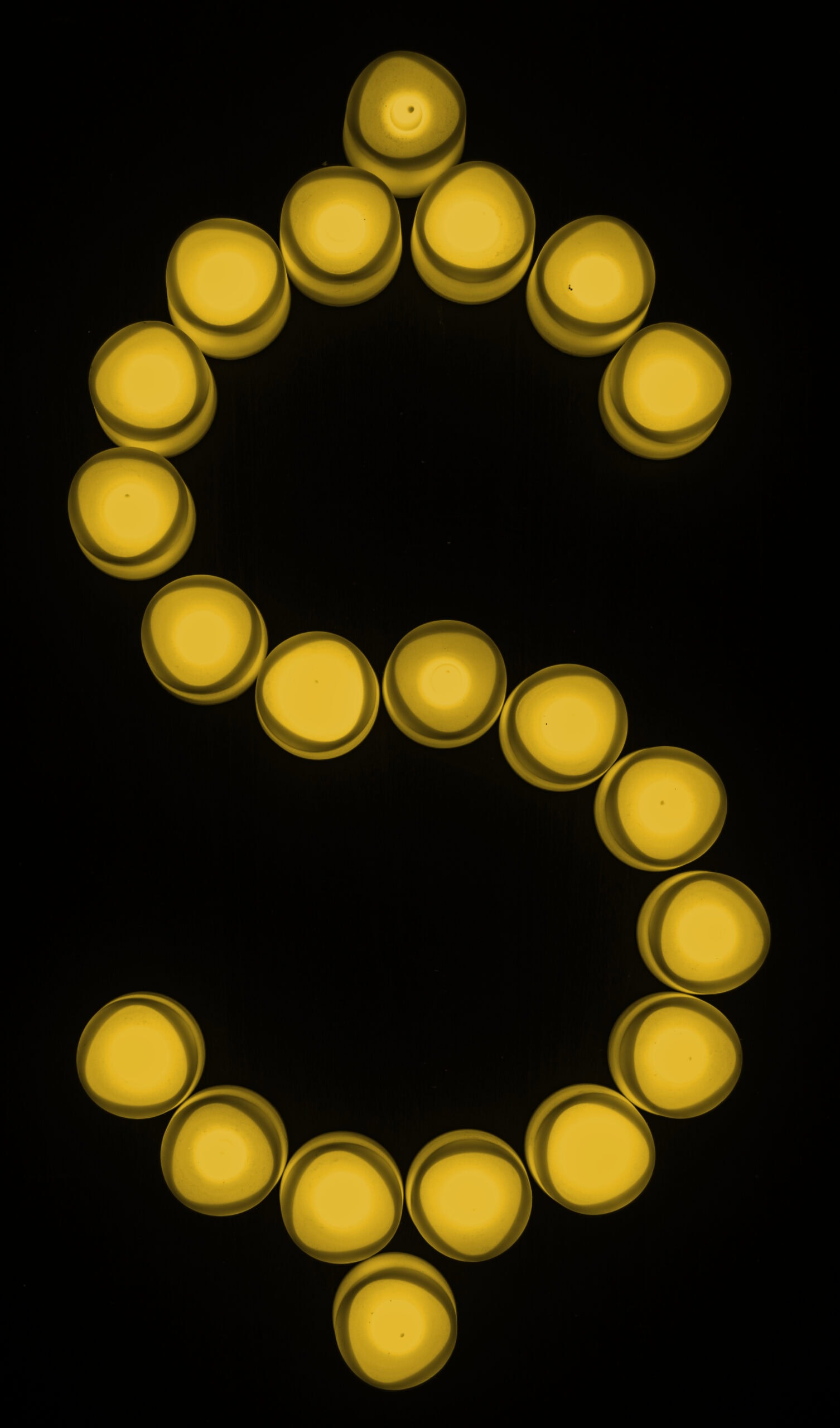Yellow candles arranged in the shape of a dollar sign ($) on a black background.